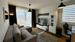 A modern living room with a sofa, a glass coffee table, a flat-screen TV, and a dining area with a chair and a cabinet. - Apartment Restart in Zadar (Zadar)