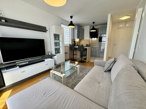 Ein modernes Wohnzimmer mit Flachbildfernseher, einem Glastisch und einem grauen Sofa.