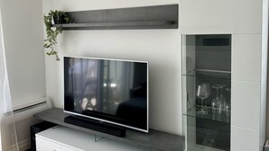 A modern living room with a flat-screen TV, a glass coffee table, and a white cabinet with glass doors. - Apartment Restart in Zadar (Zadar)