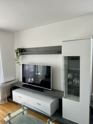Ein modernes Wohnzimmer mit Flachbildfernseher, Glastisch und weißem Schrank mit Glastüren.