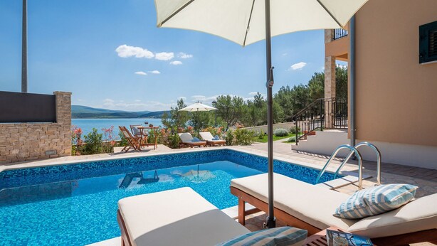 Ein Poolbereich mit Liegestühlen, einem kleinen Pool und Blick aufs Meer.