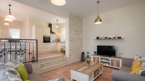 Ein modernes Wohnzimmer mit Fernseher, Sofa, Couchtisch und Essbereich mit Stühlen und Geländer.