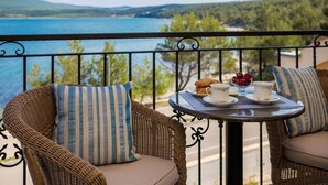 Ein Balkon mit Korbmöbeln, einem Tisch mit einem Croissant, einer Tasse und einer Schale mit Obst.