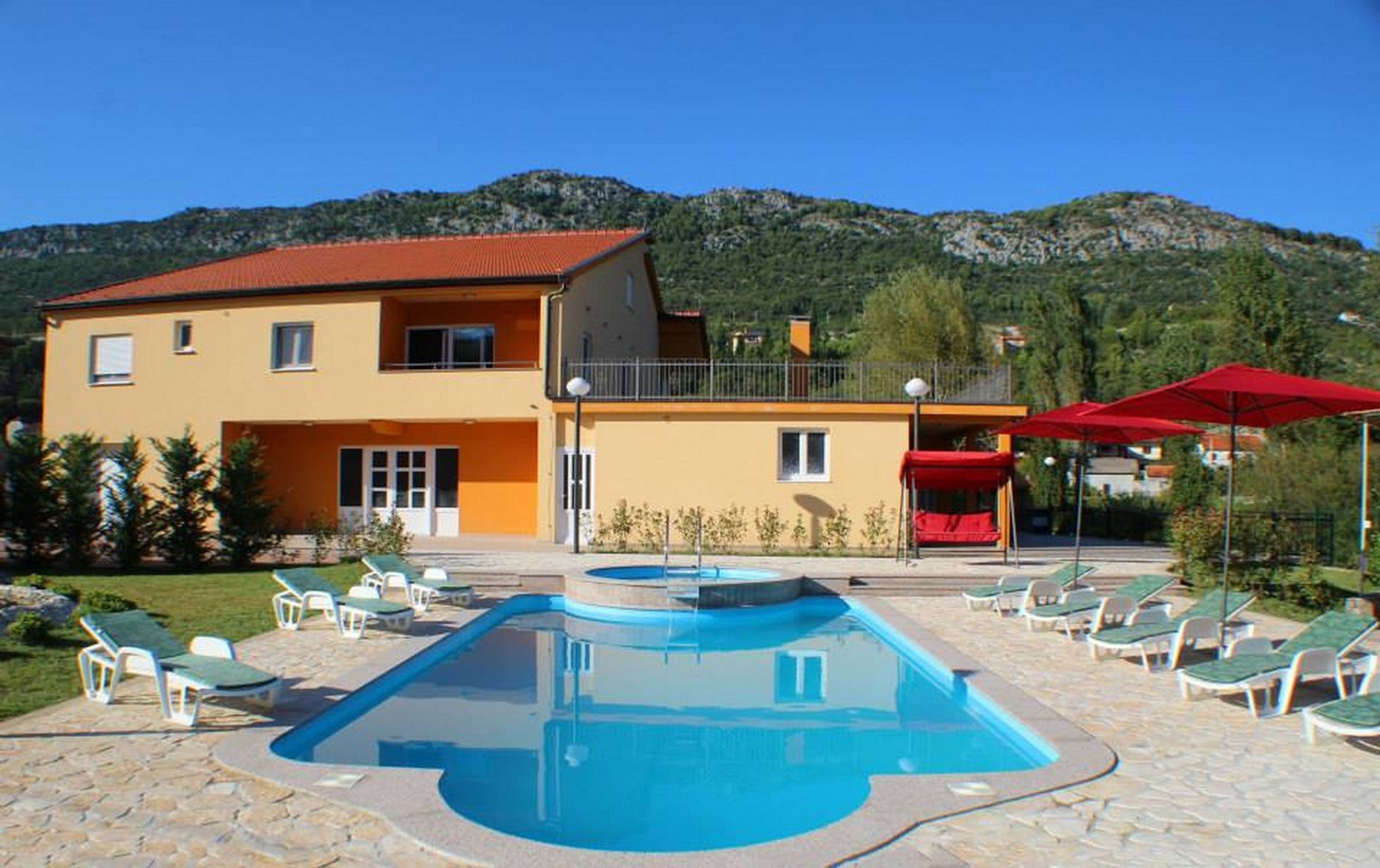 Un edificio a due piani con piscina, area salotto esterna e montagne sullo sfondo.