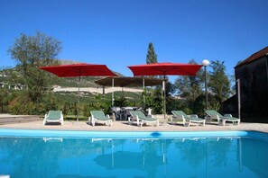 A swimming pool with lounge chairs and red umbrellas. - Holiday Home Nadalina (Vrgorac)