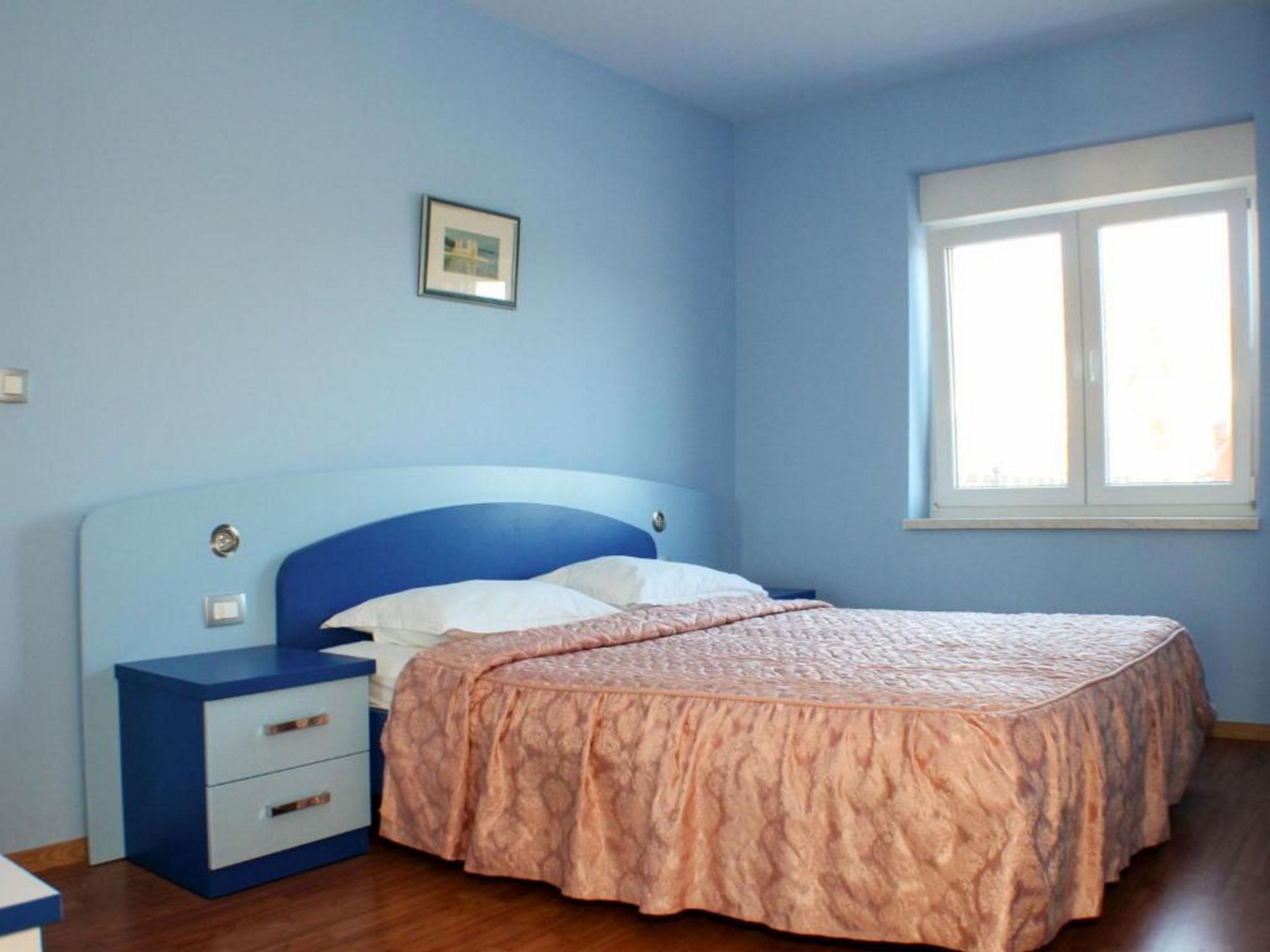 Ein Schlafzimmer mit einem Einzelbett, einem Nachttisch, einer Kommode und einem Fenster.