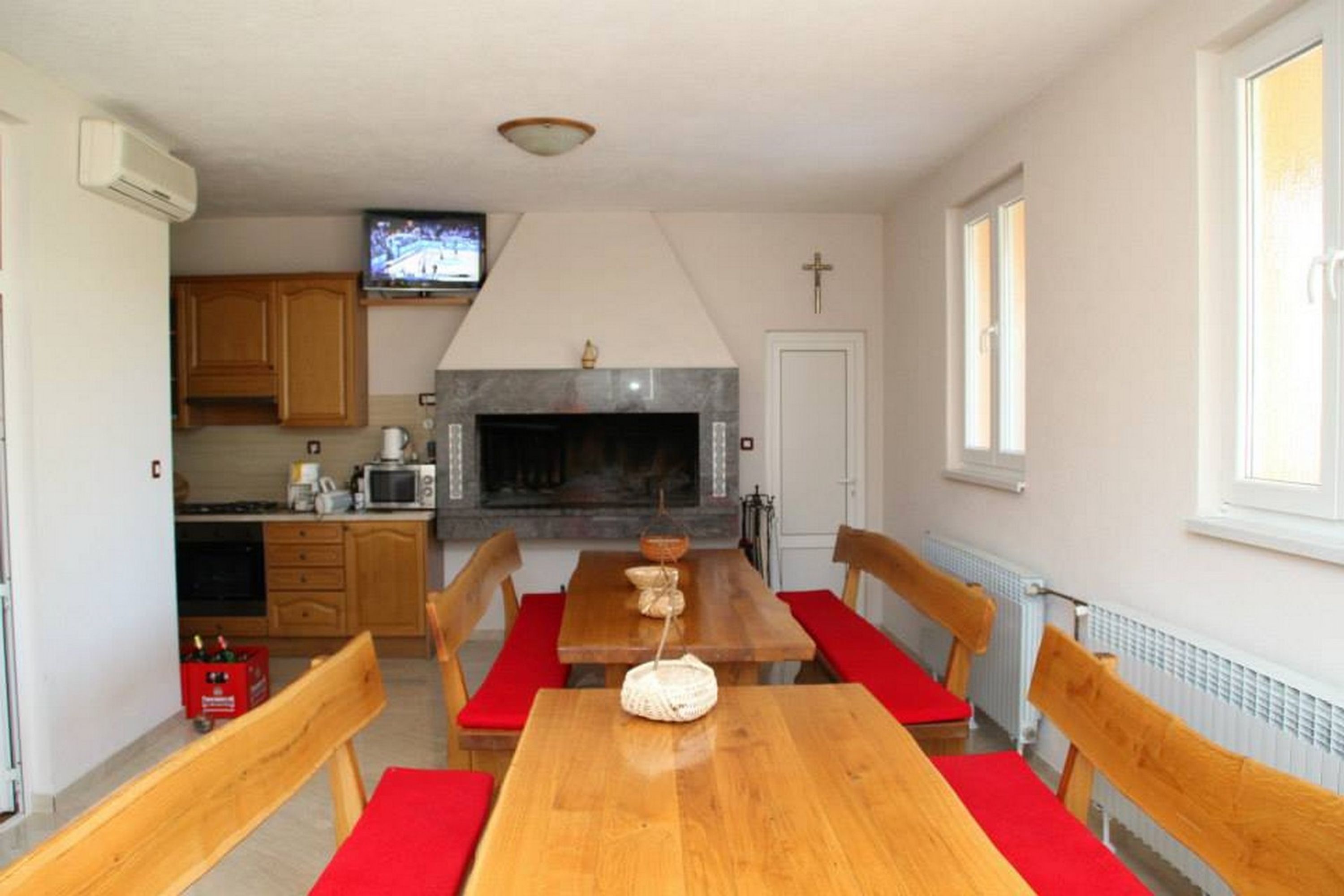 Un coin repas avec une table et des chaises en bois, une cheminée, un téléviseur et, au fond, une cuisine.
