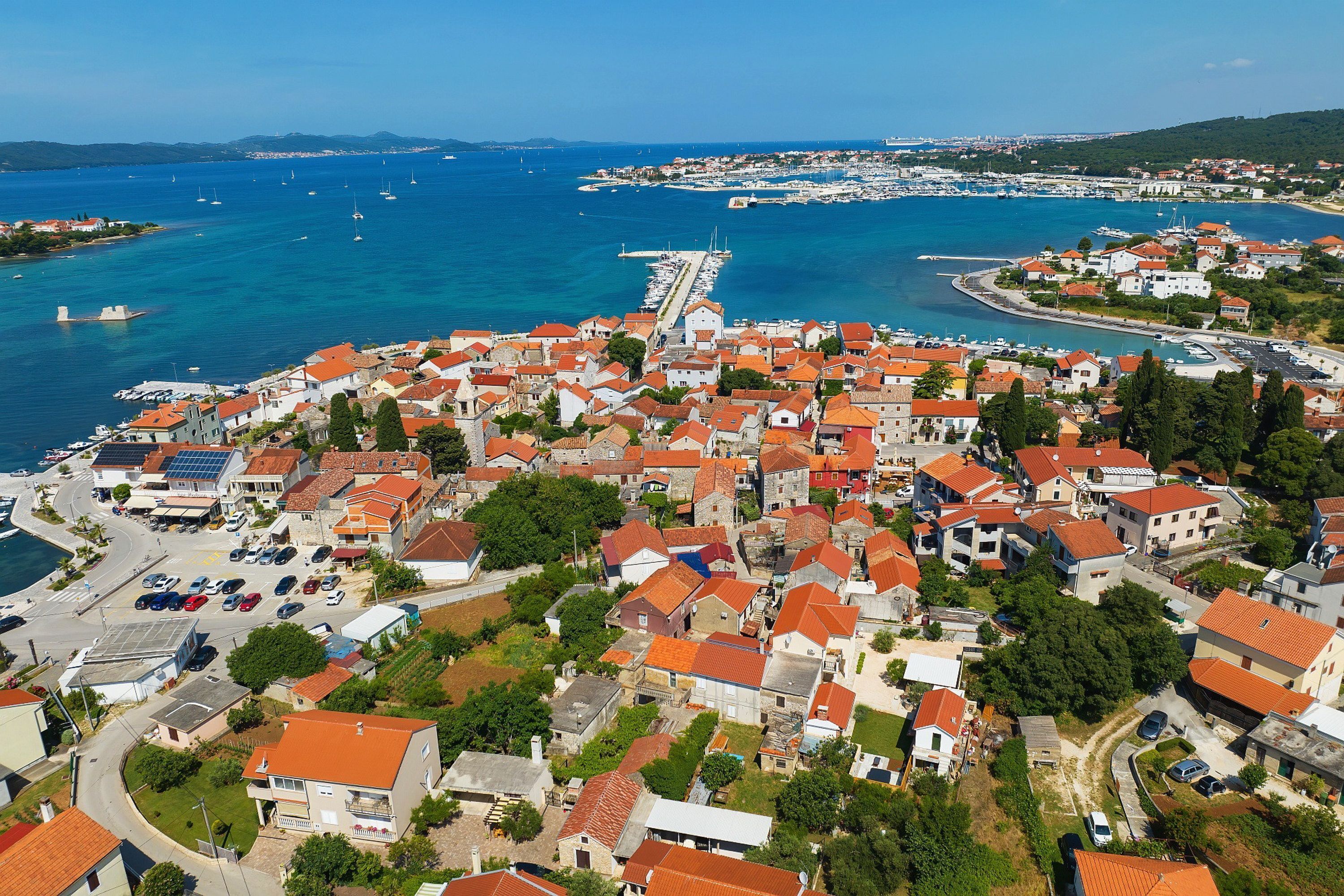 A coastal town with red-roofed buildings, a marina, and a pier extending into the sea.