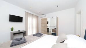 Una habitación de hotel moderna con una cama, un televisor de pantalla plana, una mesita de noche con una planta y un espejo.