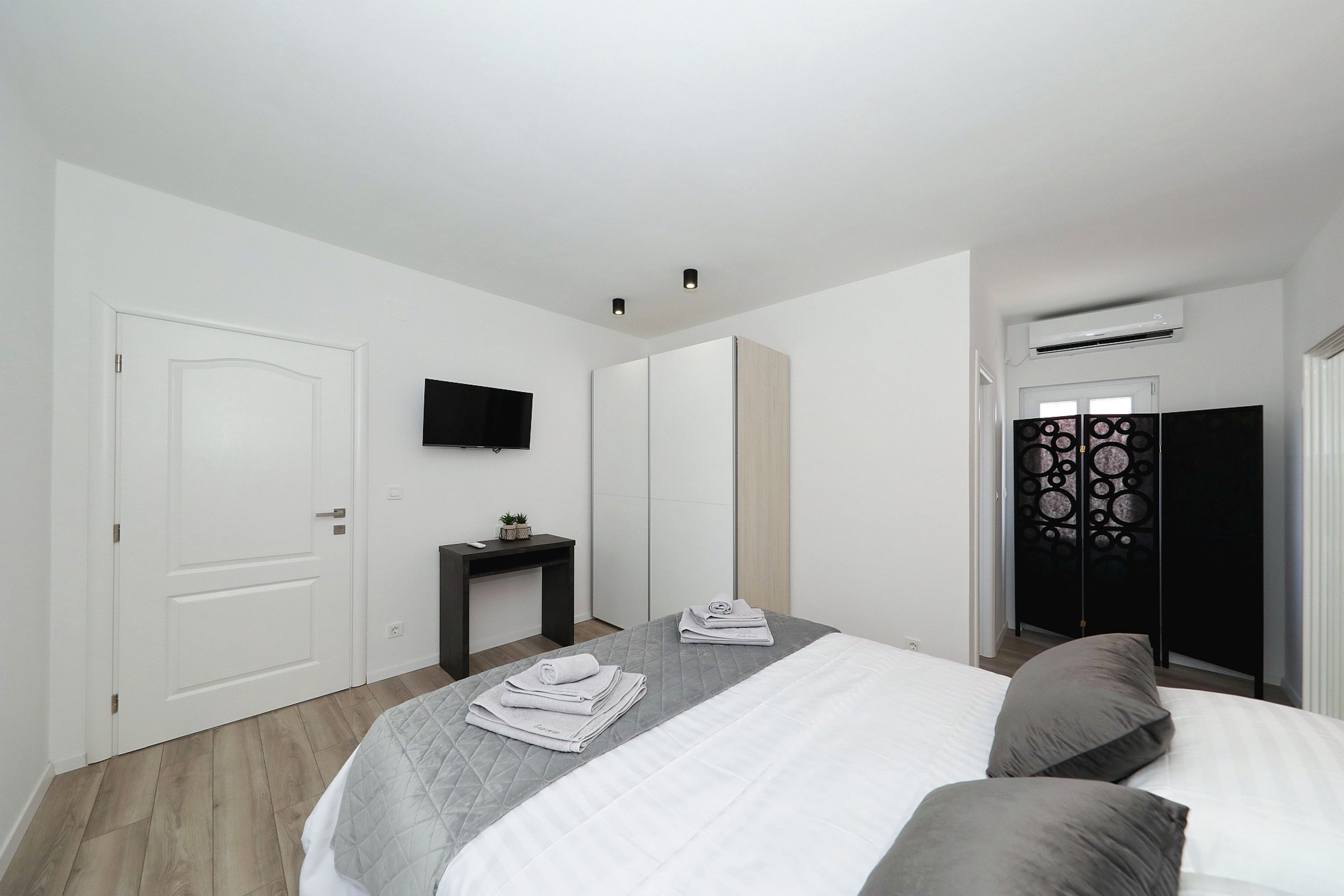 Un dormitorio con una cama, un televisor en la pared, una mesita con una planta y un armario.