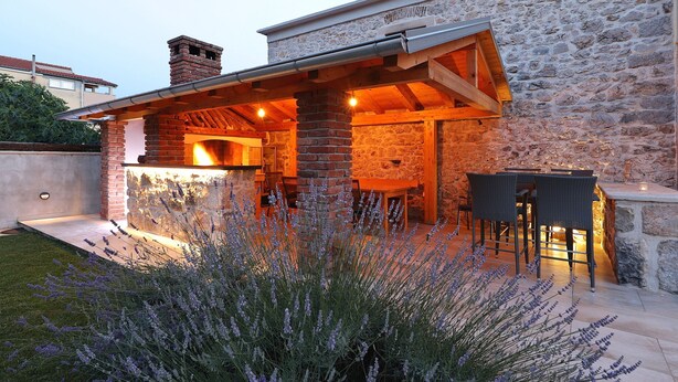 Un edificio de piedra con chimenea de ladrillo, mobiliario exterior y un césped bien cuidado.