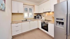 Een moderne keuken met witte kasten, een roestvrijstalen koelkast, een magnetron, een koffiezetapparaat en een oven.