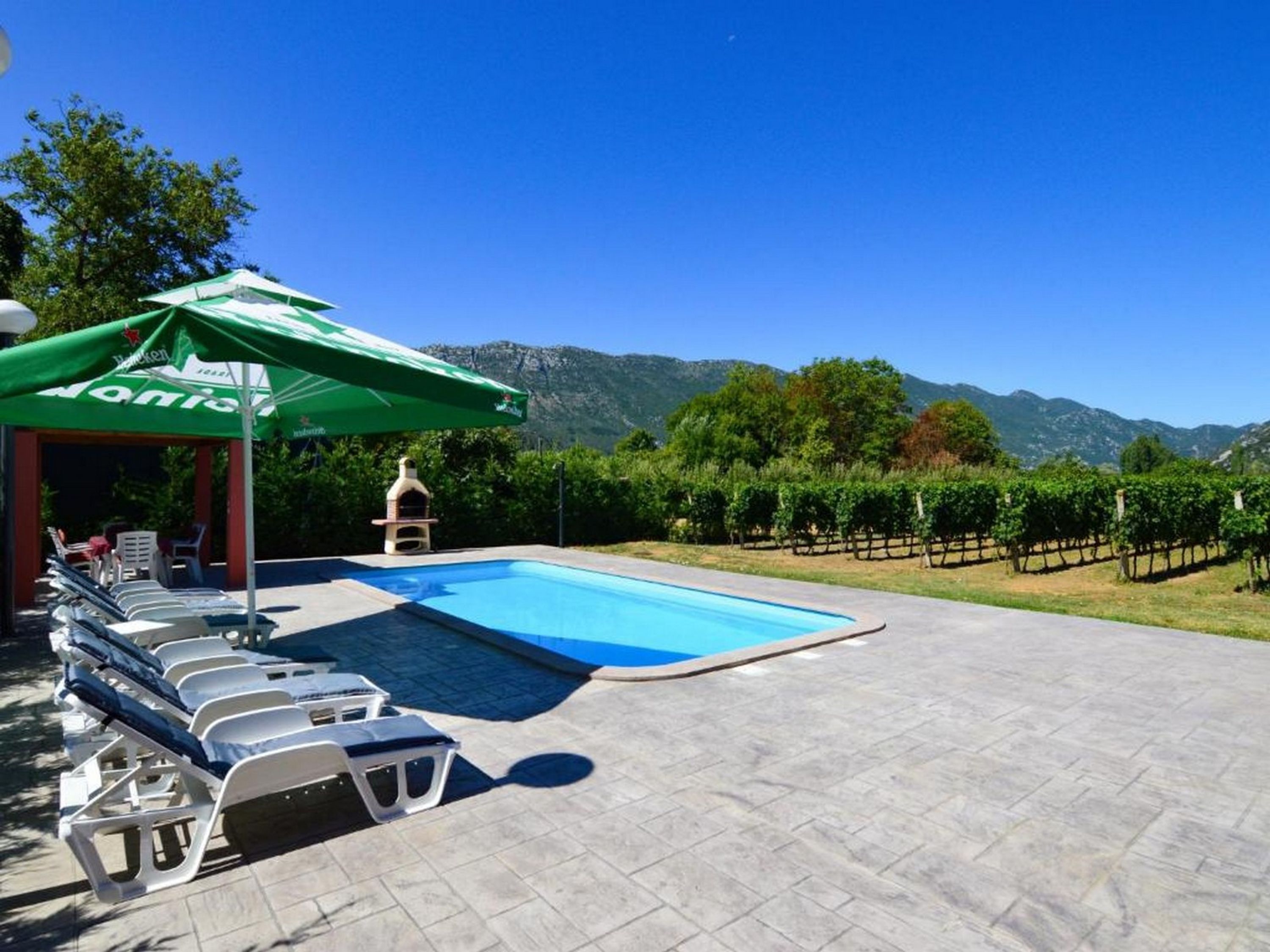 A pool area with lounge chairs, a barbecue grill, and a view of vineyards and mountains.
