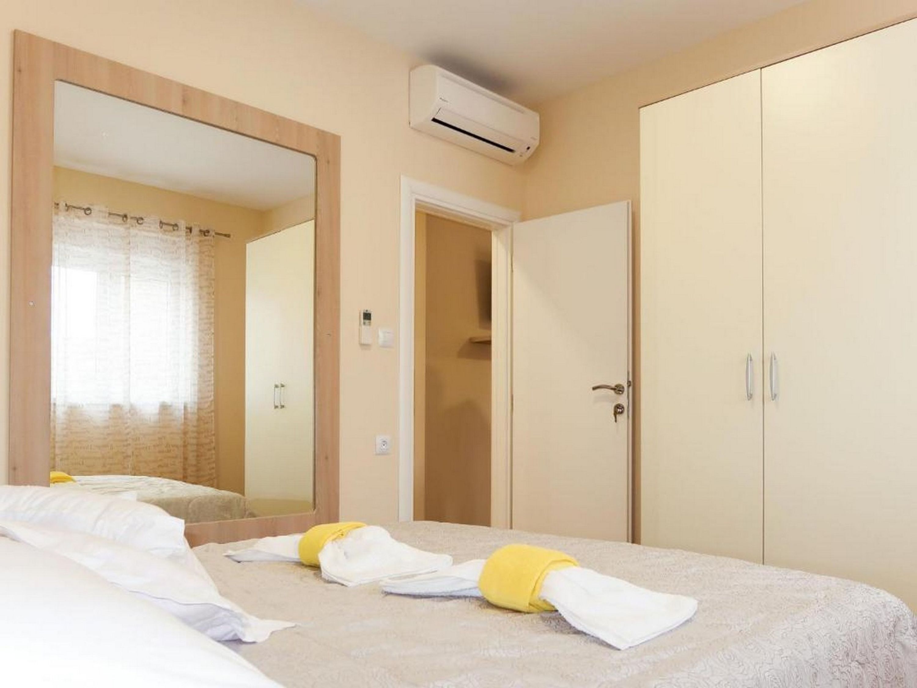 A hotel room with a bed, a wardrobe, a mirror, and an air conditioning unit.