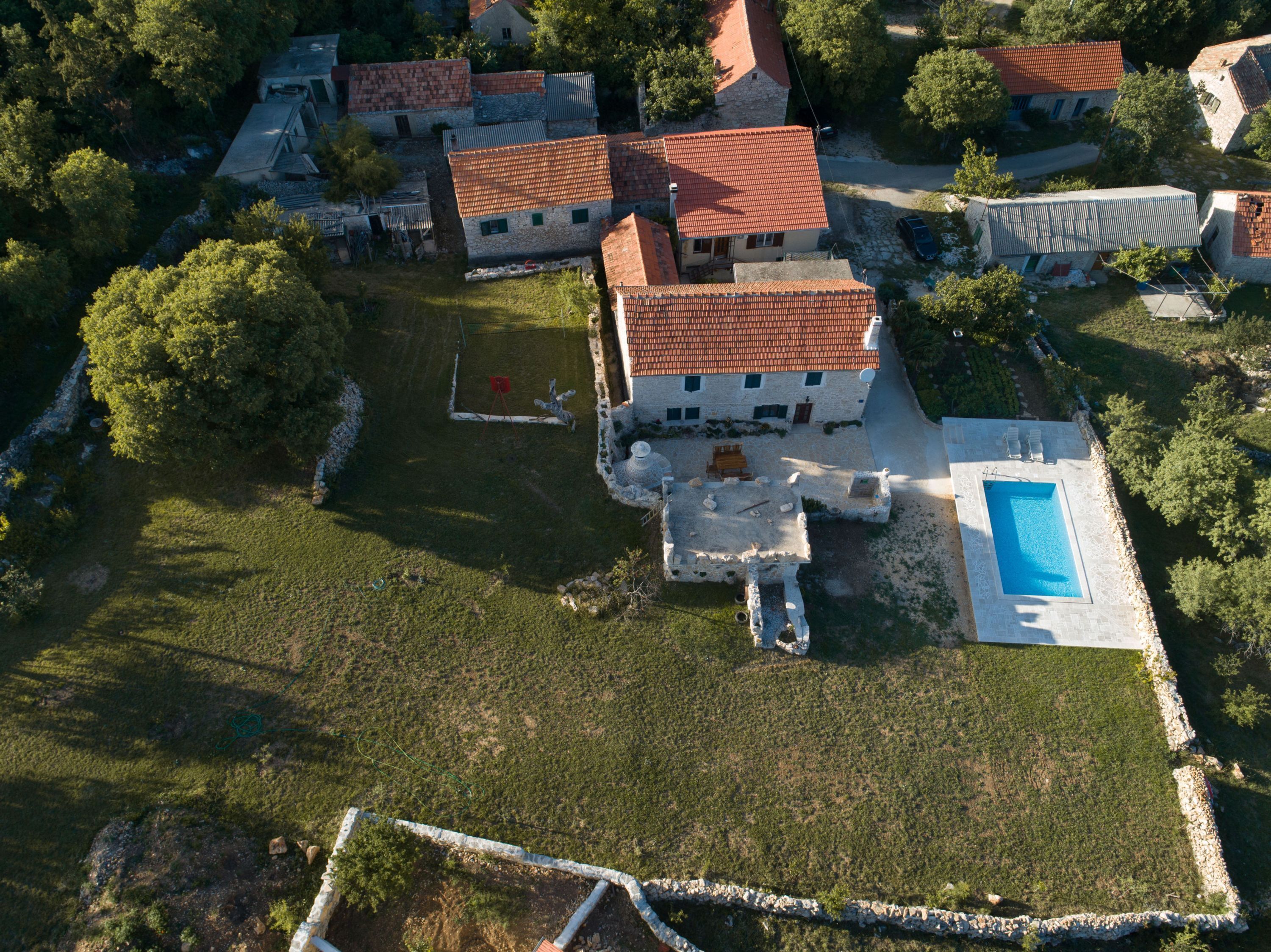 An aerial view of a residential area with stone buildings, a swimming pool, and surrounding greenery.