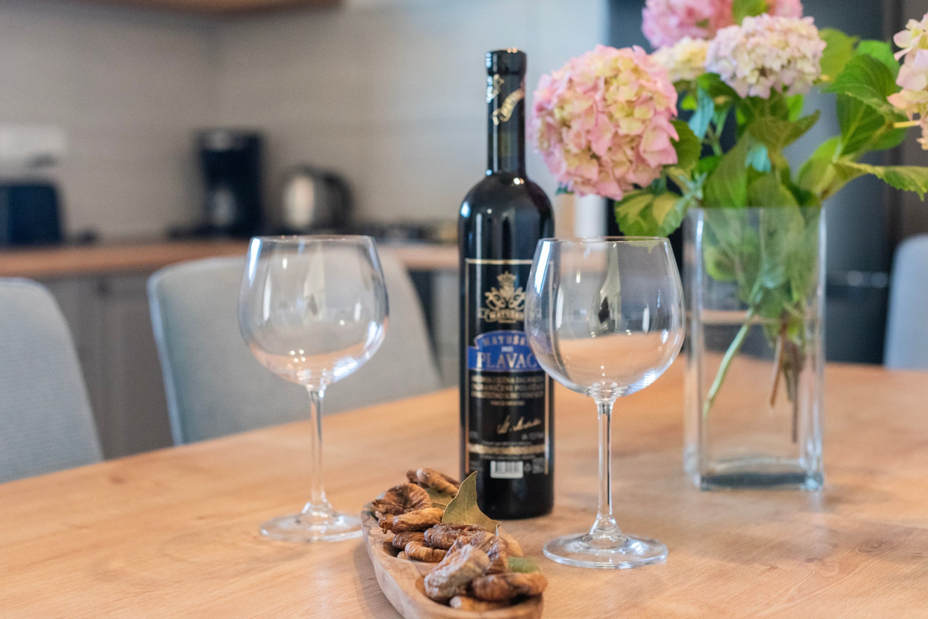 Una mesa de madera con dos copas de vino vacías, una botella de vino y un cuenco de frutas secas.