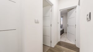 Un corridoio con pareti bianche e pavimento in legno che conduce a una camera da letto con un letto e una finestra.