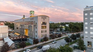 Un hotel moderno con facciata in vetro, un parcheggio e vista sullo skyline circostante al tramonto.