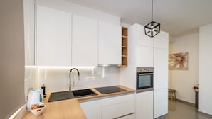 Une cuisine moderne avec des meubles blancs, un plan de travail en bois, un four encastré et un luminaire suspendu noir en forme d’hexagone.