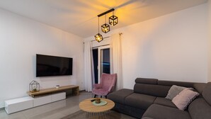 Un salon moderne avec un téléviseur à écran plat, une table basse ronde, un canapé et un fauteuil rose.