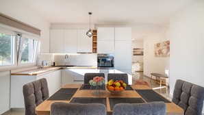 Une cuisine moderne avec des meubles blancs, un plan de travail en bois et un coin repas comprenant une table et des chaises.