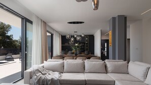 A modern living room with a large sectional sofa, a wooden coffee table, and a dining area with a dark-colored kitchen in the background. - Villa Santa With Heated Pool (Pakostane)