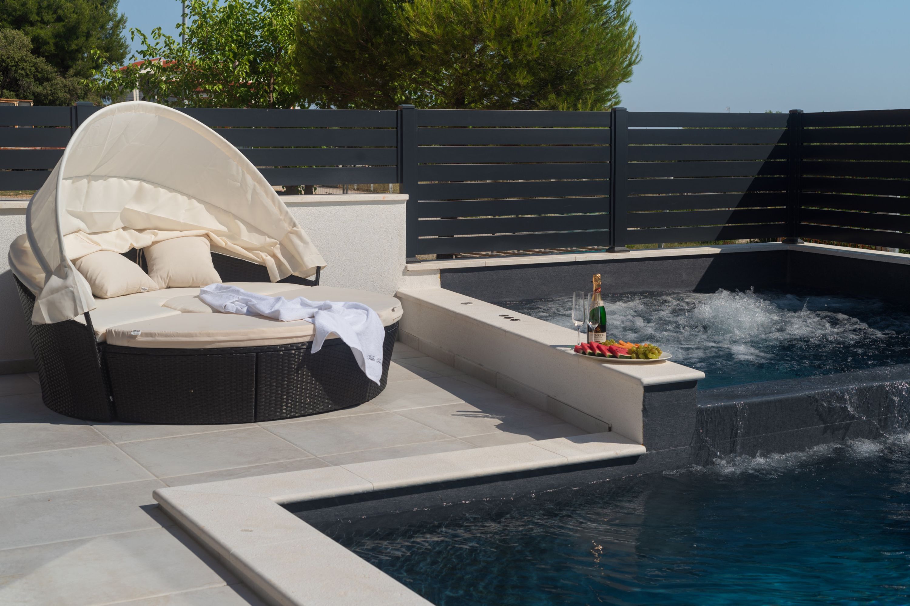 Un espace aménagé au bord de la piscine, avec un fauteuil abrité et une bouteille de champagne.