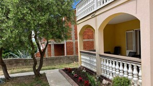 A building with a yellow facade, a balcony with white balustrades, and a garden area with various plants and flowers. - Holiday Home Bella 1 Bella 2 (Povljana)