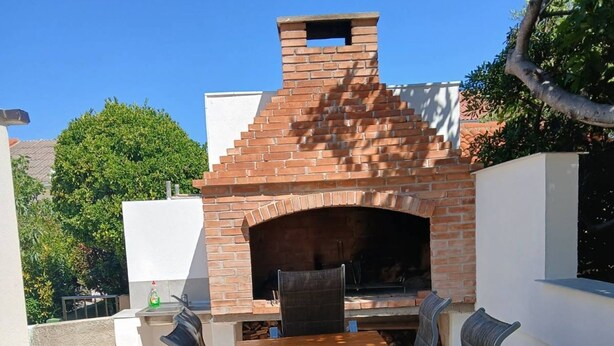 An outdoor brick oven barbecue area with a wooden table and chairs. - Holiday Home Bella 1 Bella 2 (Povljana)