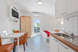Une cuisine compacte avec un coin repas, un téléviseur fixé au mur et une porte coulissante donnant sur un balcon.