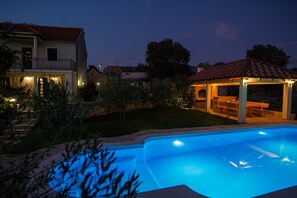 En swimmingpool med ett uteområde, en möblerad plats under tak och ett hus med en balkong.