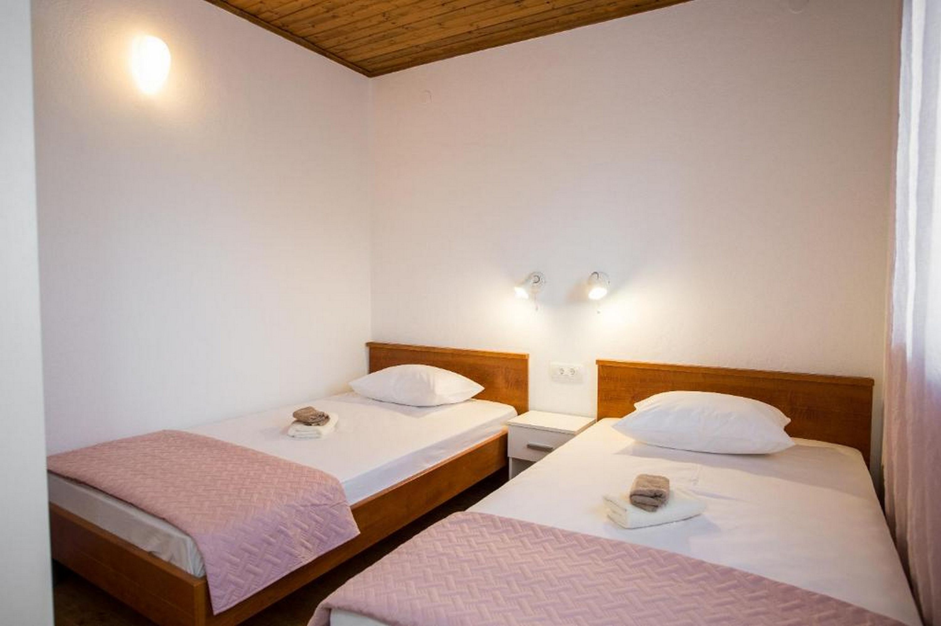 Una habitació amb dos llits individuals, cadascun amb un capçal de fusta, roba de llit blanca i una petita taula de nit. Hi ha llums penjades a la paret sobre cada llit.