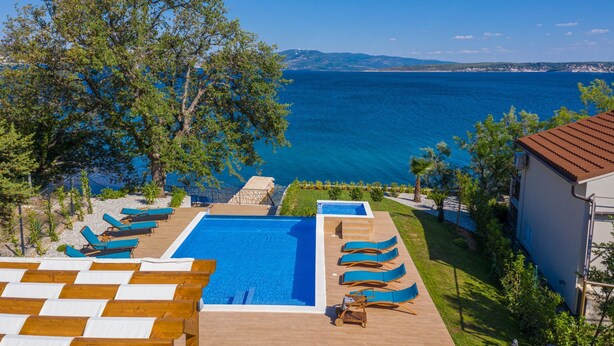 A pool area with lounge chairs and a view of the sea. - Beachfront Villa Promenada (Posedarje)
