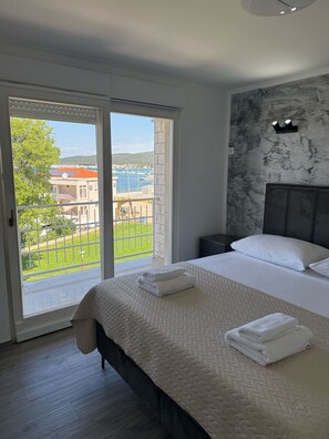 Een slaapkamer met een bed, een nachtkastje en uitzicht op een jachthaven door een schuifdeur.