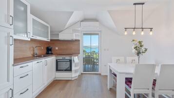 A modern kitchen with white cabinetry, a built-in oven, and a dining area with a white table and chairs.