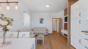 A modern kitchen with white cabinets, a wooden floor, and a dining area with a table and chairs.
