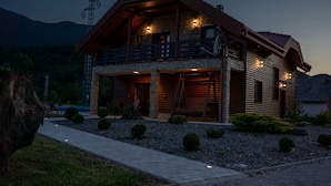 Una cabaña de madera de dos pisos con cimientos de piedra, un balcón y una entrada bien iluminada.