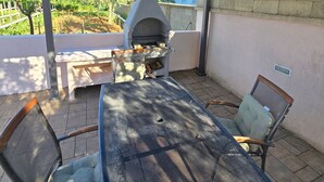 Eine Terrasse im Freien mit Grill, Tisch und Stühlen.