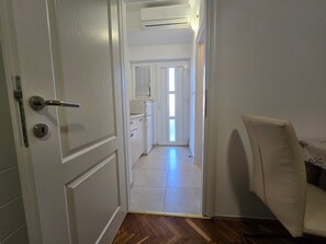 A narrow hallway with white walls, a wooden floor, and a white door with a silver handle. - Studio Apartment Vita (Nin)