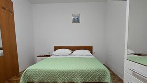 Ein Schlafzimmer mit Bett, Holzboden, weißen Wänden, einem kleinen Bild an der Wand und einem Kleiderschrank.