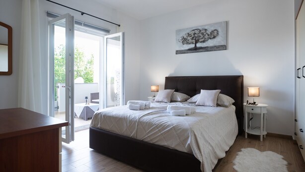 A bedroom with a bed, bedside tables, a nightstand, a white rug, and a painting on the wall. - Holiday Home Lantina With Pool (Novigrad)