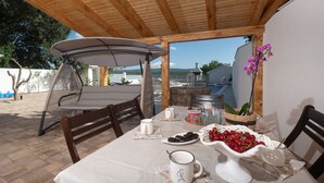 A wooden pergola with a table set for dining, featuring a white tablecloth, chairs, and a table with a bowl of cherries and a pitcher. - Holiday Home Lantina With Pool (Novigrad)