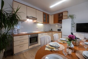 A modern kitchen with wooden cabinets, a stainless steel oven, and a dining area set for four with white chairs and a table set with plates, glasses, and a vase with flowers. - Holiday Home Lantina With Pool (Novigrad)