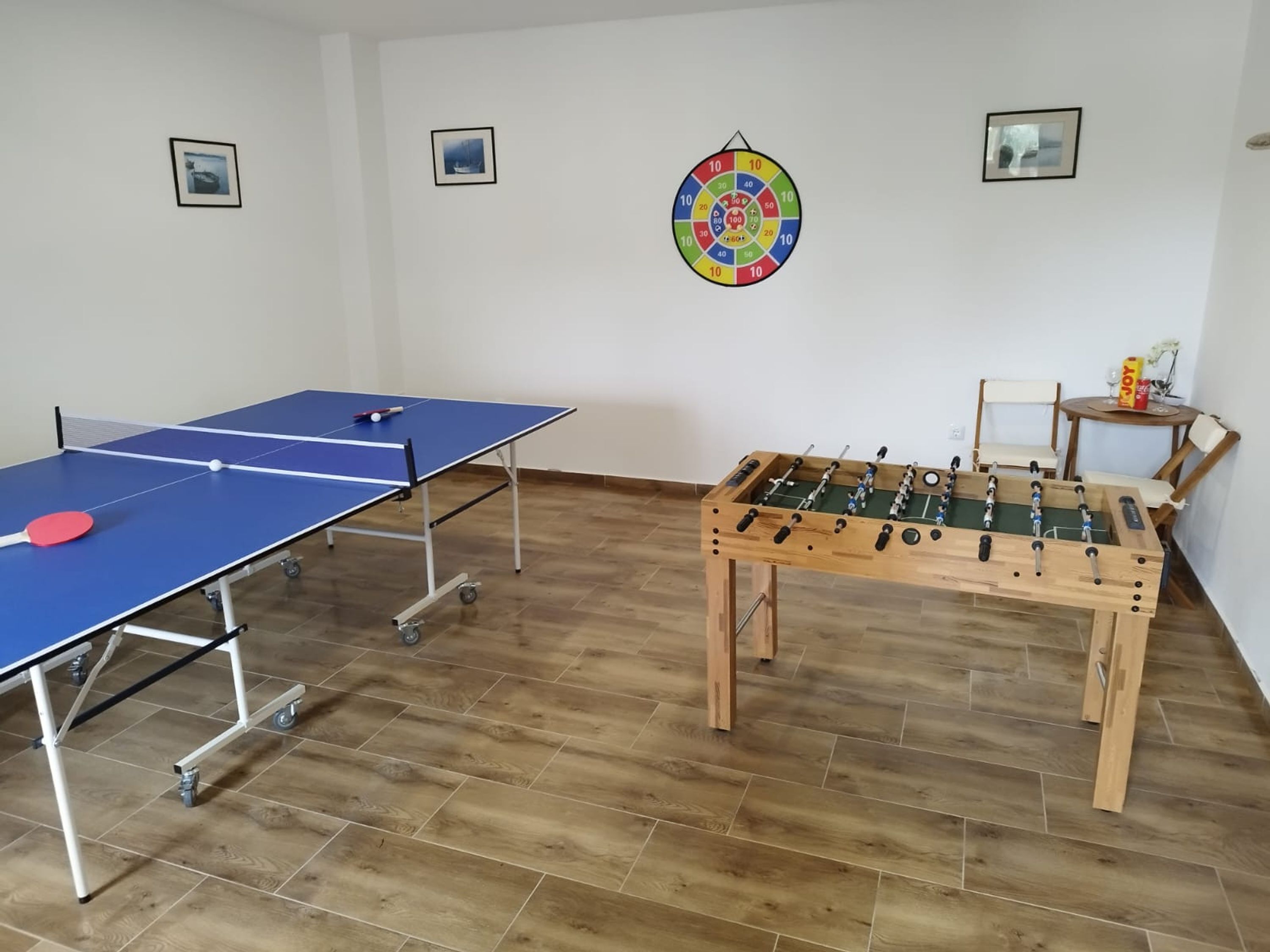 A room with a ping pong table, a foosball table, and three framed pictures on the wall.