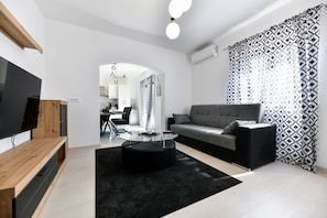 Ein stilvolles Wohnzimmer mit Fernseher, Sofa, Couchtisch und gemusterten Vorhängen.