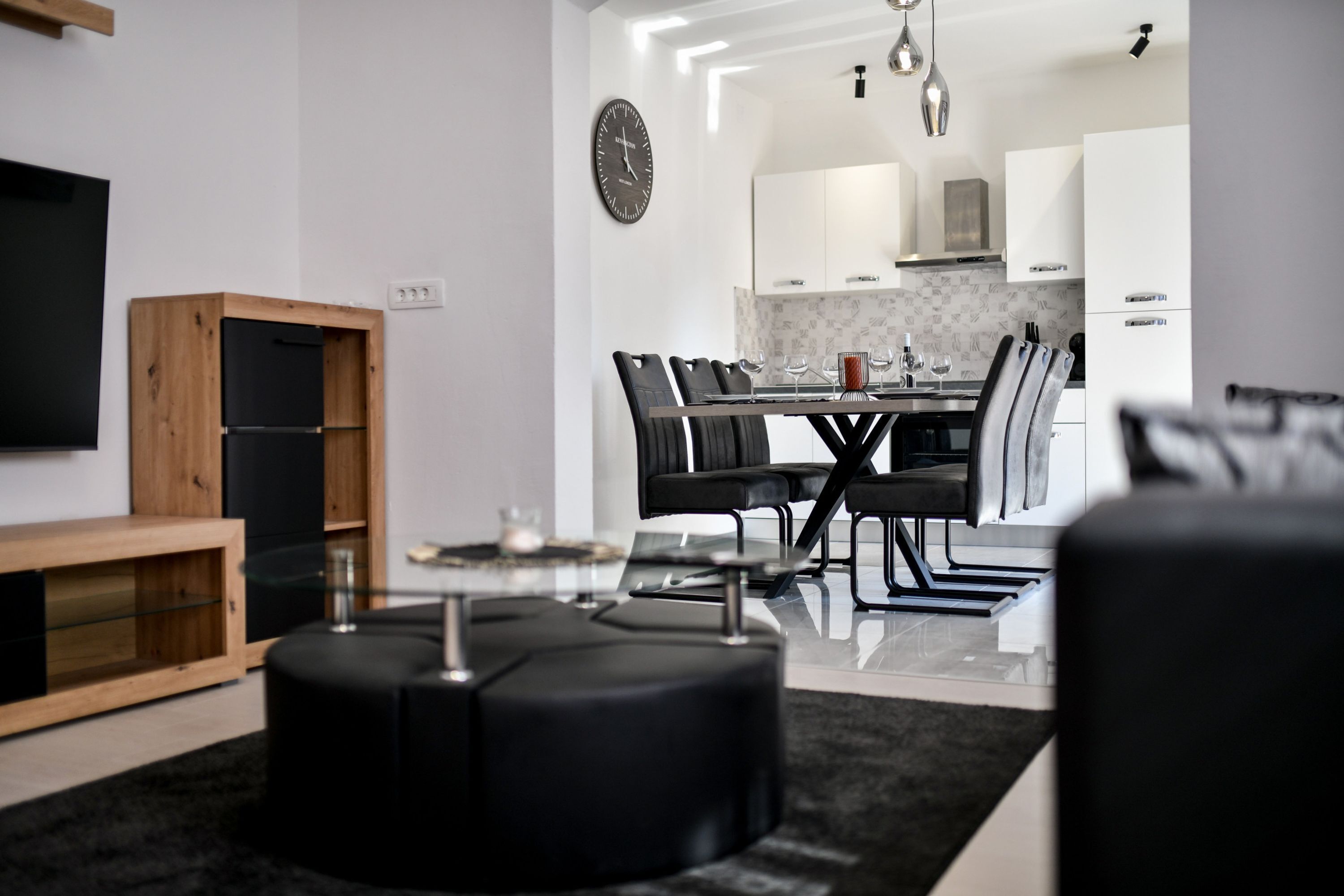 A modern kitchen with white cabinets, a dining table with chairs, and a black ottoman.