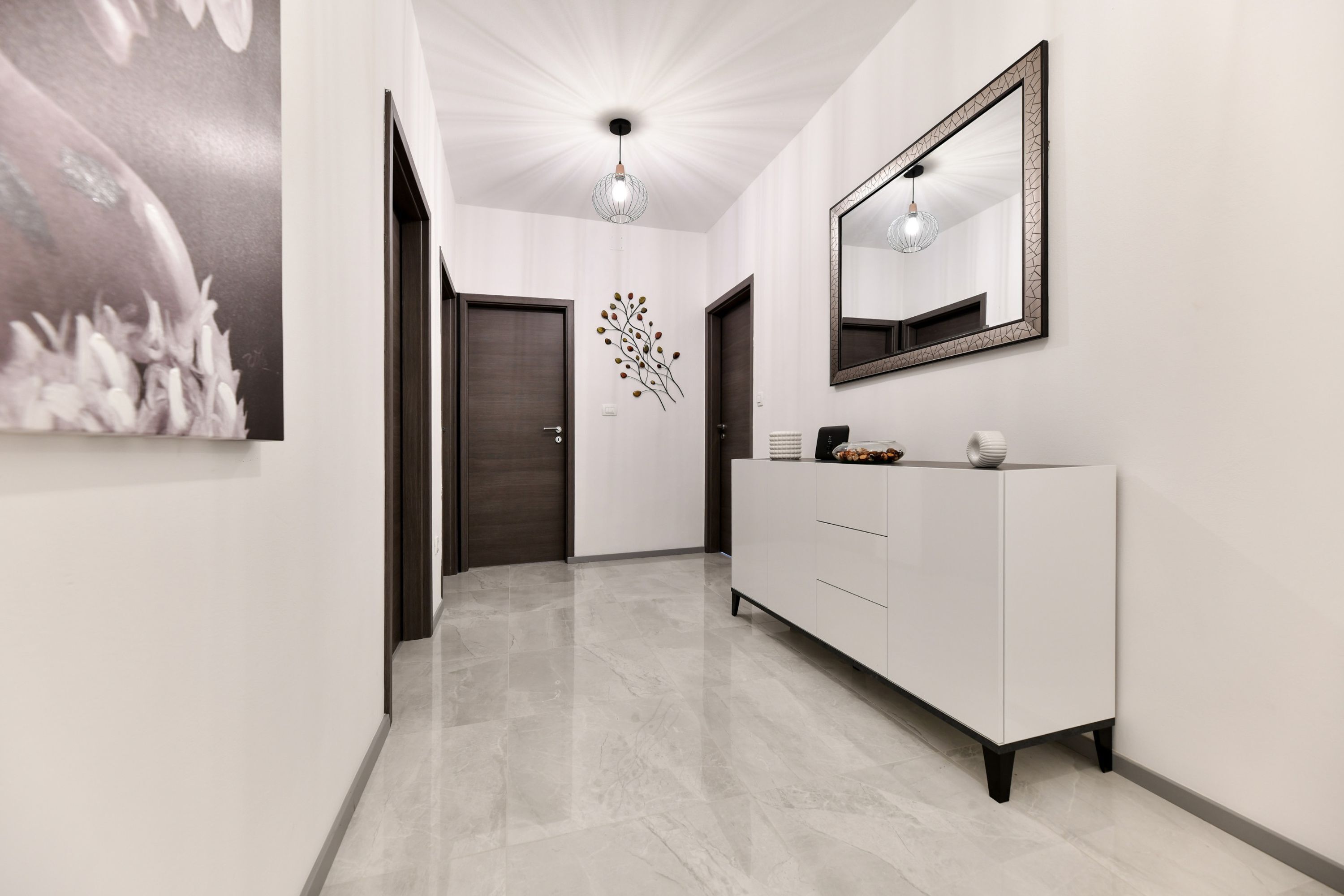 A hallway with a white cabinet, a mirror, and a wall art piece.