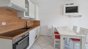 A modern kitchen with white cabinets, a wooden countertop, a built-in oven, and a dining area with a white table and red chairs. - Superior Studio Tania 16 (Sveti Filip i Jakov)