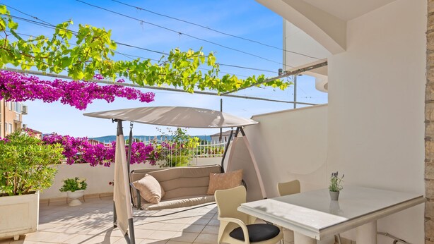 A sunlit patio with a white table, beige sofa, and a hanging chair. - Superior Studio Tania 16 (Sveti Filip i Jakov)