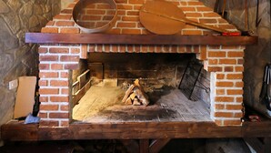Ein Kamin aus Ziegelsteinen mit einem Holzschild darüber, eine Steinwand und ein Holztisch mit einem Korb und einem Topf.